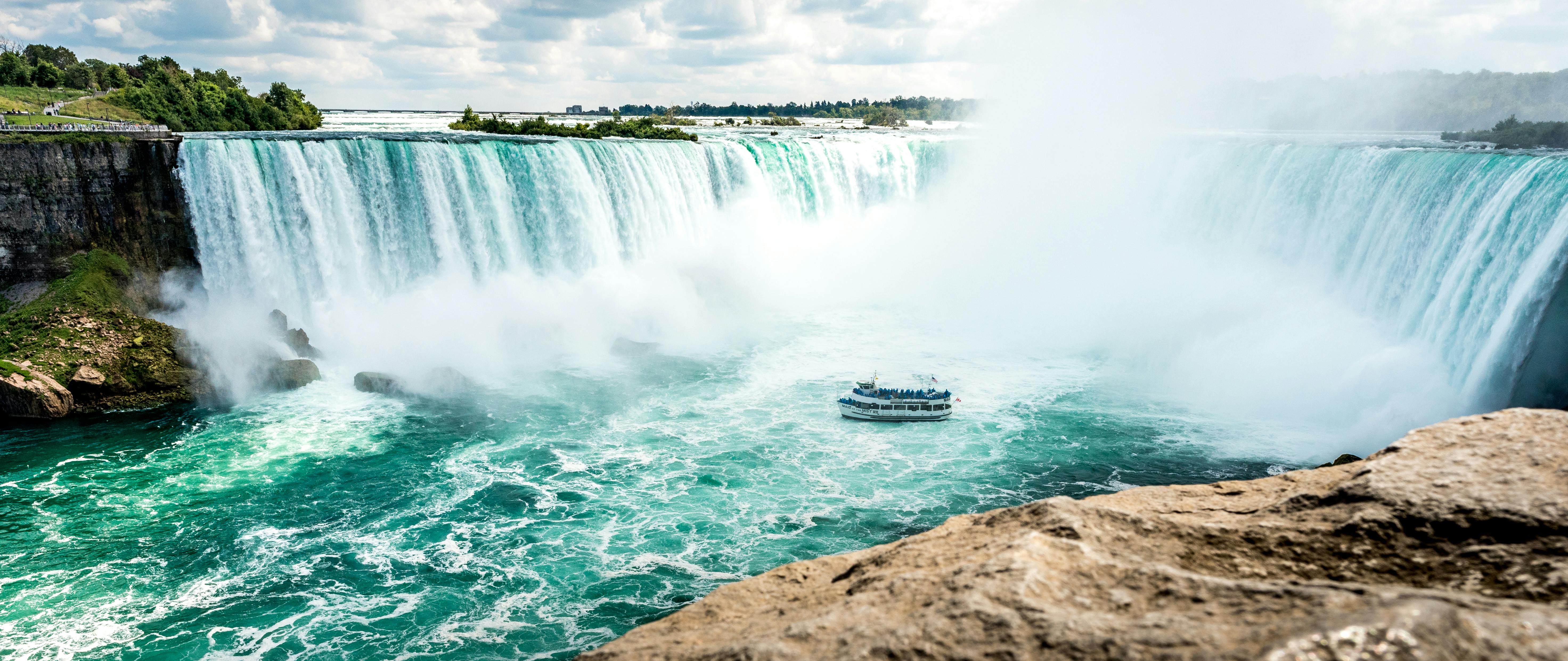 Niagara Falls Horseshoe Falls with tour boat cruising through mist on a day trip from Toronto.