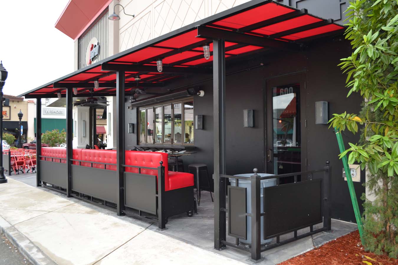 Modern red and black commercial canopy with outdoor seating area at a restaurant storefront.
