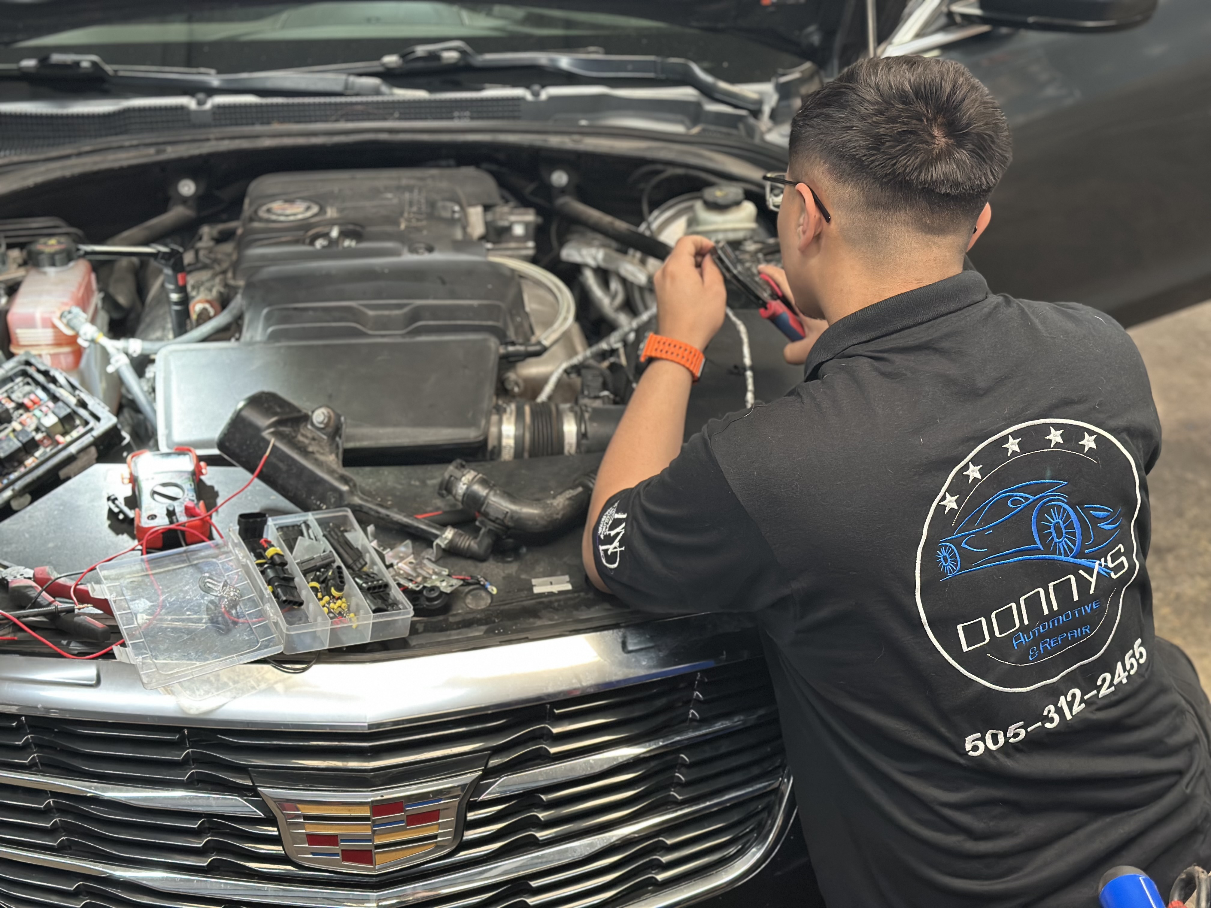 "A mechanic at Donny's Automotive LLC wearing a branded shirt with the shop's logo and contact number, working at a well-organized tool station filled with professional equipment. The image highlights the expertise and professionalism of the team." "A mechanic at Donny's Automotive LLC wearing a branded shirt with the shop's logo and contact number, working at a well-organized tool station filled with professional equipment. The image highlights the expertise and professionalism of the team."