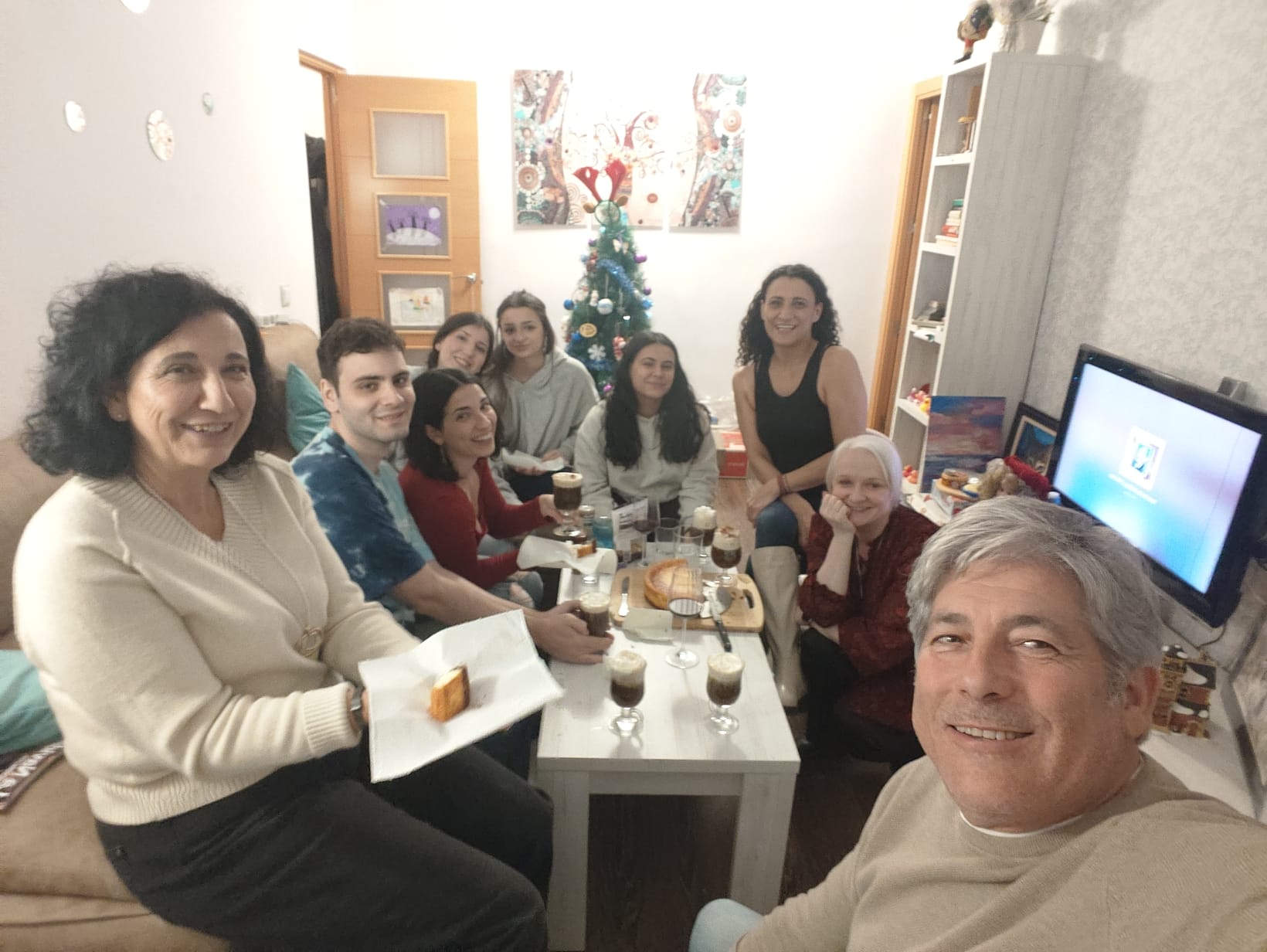 A family of 10 people sitting around a table sharing coofee and cake while deoorating a Christmas tree A family of 10 people sitting around a table sharing coofee and cake while deoorating a Christmas tree