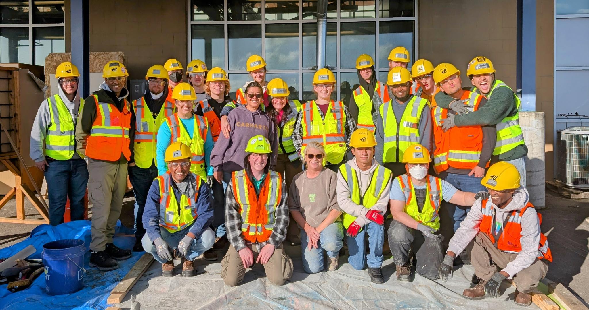 A group of people smiling in construction vests and hard hats.