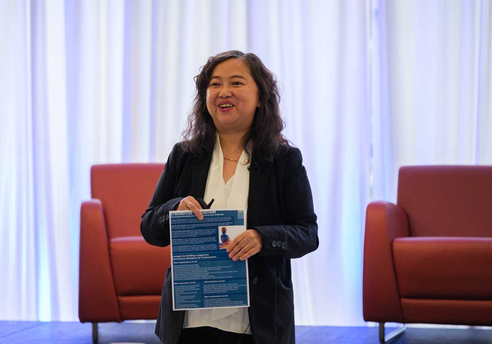 A women holding a blue flyer presenting on stage.