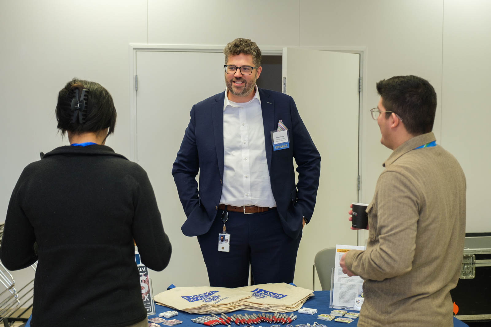 A man in a blazer standing behind a table.