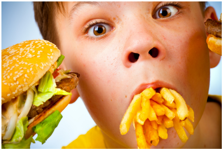 young boy holding a fast food burger with a mouth full of french fries