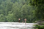 My sons and husband are standing in the water near the edge of a waterfall with trees surrounding the water.
