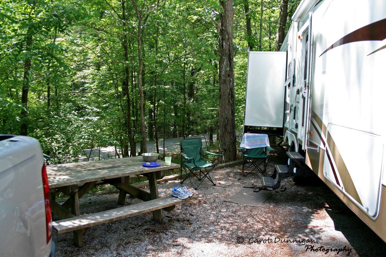View of our tree shaded campsite at Fall Creek Falls State Park. It shows part of our 5th Wheel RV and our picnic table with a couple of lawn chairs.