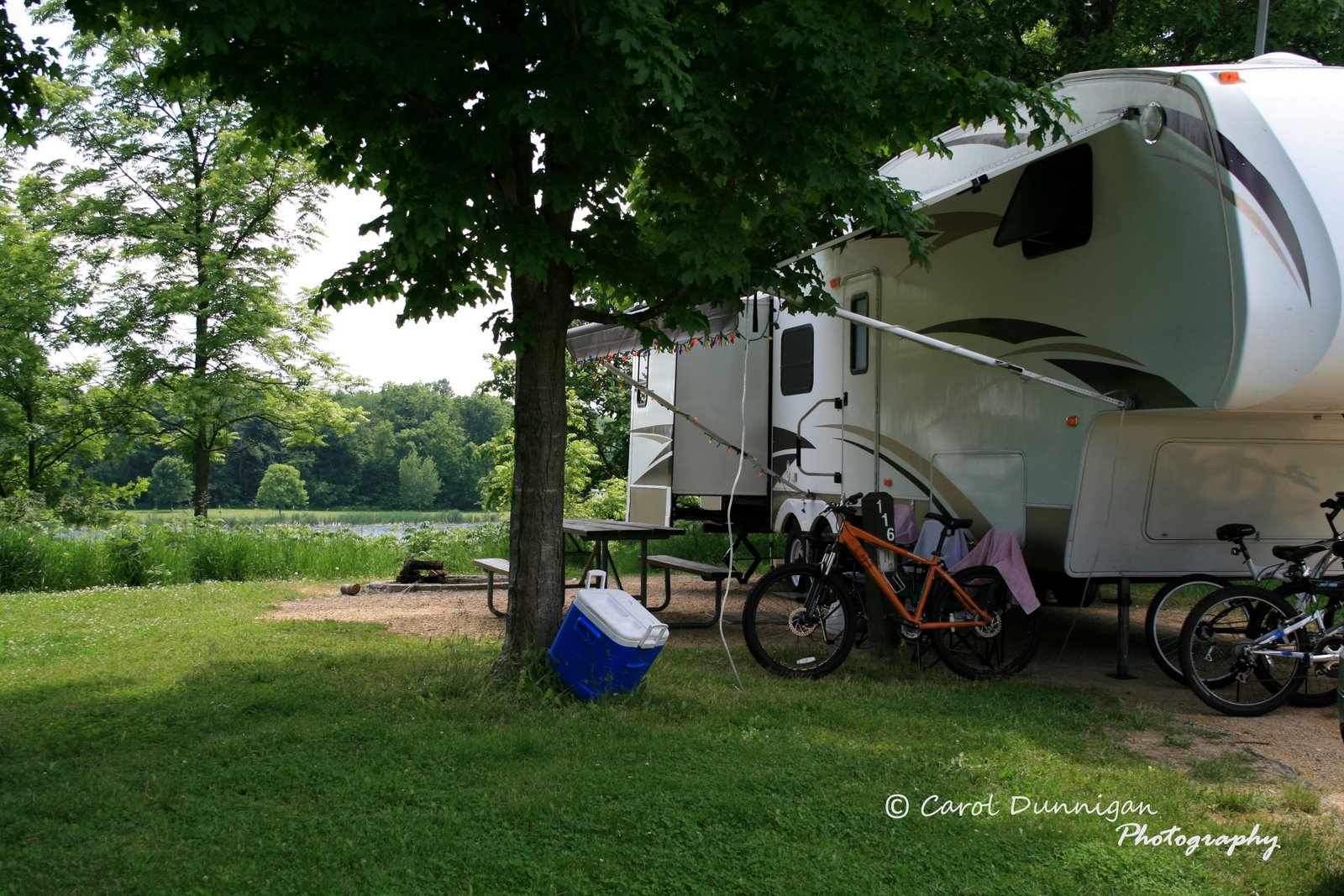 A view of our 5th Wheel RV on our grassy, shaded campsite, overlooking the lake at Shabana State Park.