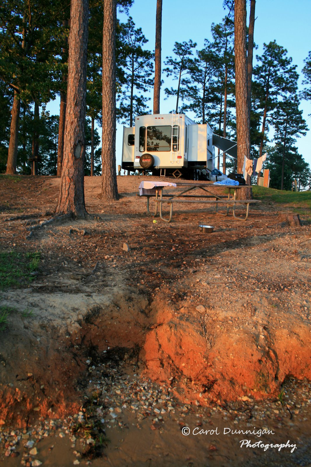 A view of our campsite in the setting sun.  The back of our 5th wheel RV is bathed in the beautiful red/orange color of sunset. I took this picture from down at the waters edge, so I'm looking up.