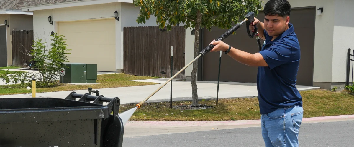Technician pressure washing a residential trash bin during professional cleaning service Technician pressure washing a residential trash bin during professional cleaning service