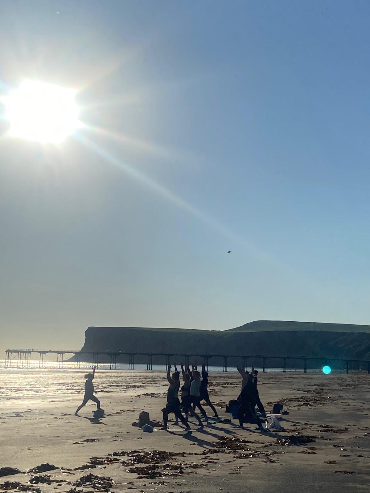 Rachel from Rogue Blossom Yoga facilitating a class on Saltburn beach with Huntcliff iand Saltburn pier in the background Rachel from Rogue Blossom Yoga facilitating a class on Saltburn beach with Huntcliff iand Saltburn pier in the background