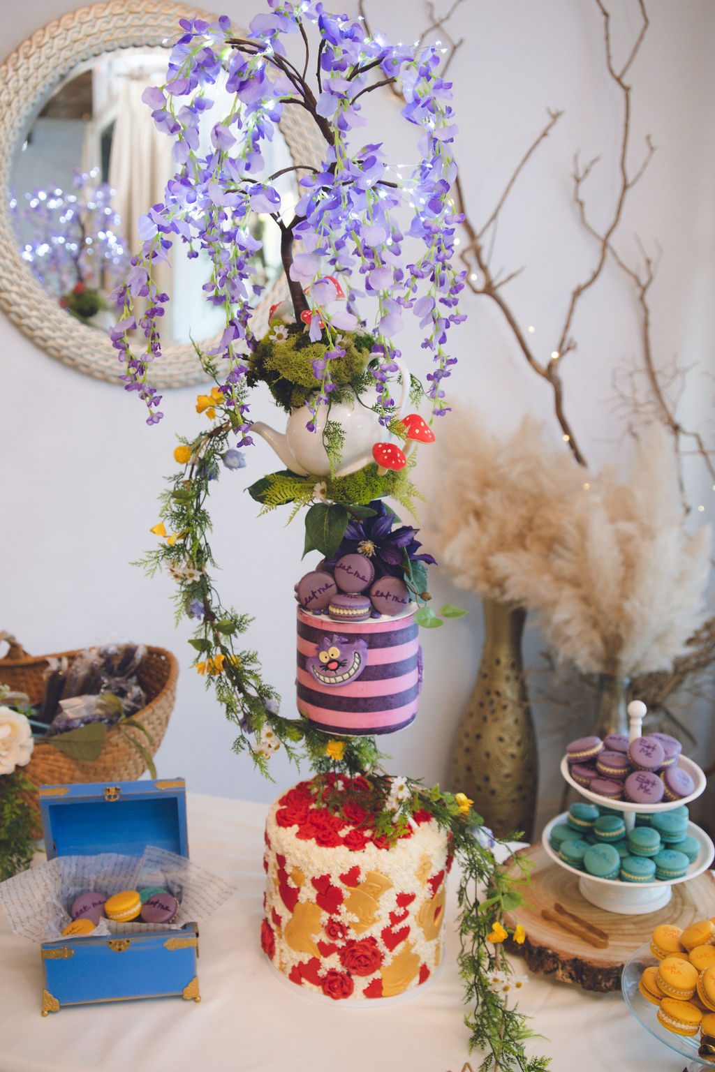 A whimsical Alice in Wonderland quinceanera dessert table featuring a Cheshire Cat cake, 'Eat Me' macarons, and colorful decor, capturing the playful spirit of an Alice in Wonderland quince theme.