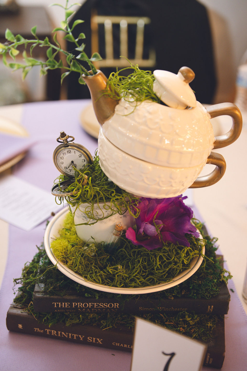 Whimsical Alice in Wonderland-themed table centerpiece featuring a teapot, pocket watch, and moss, perfect for an Alice in Wonderland quinceanera decor idea.