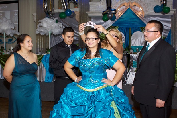 Quinceañera smiling as she receives her crown during the quinceañera program, surrounded by family members on the dance floor.