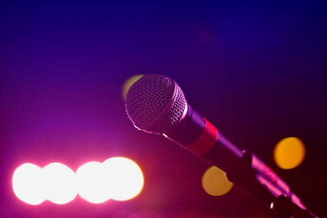 Close-up of a microphone on a stand against a vibrant background with bright stage lights. The focus on the microphone highlights the importance of holding it properly during a quinceañera speech, ensuring it is not held too low for clear audio projection.