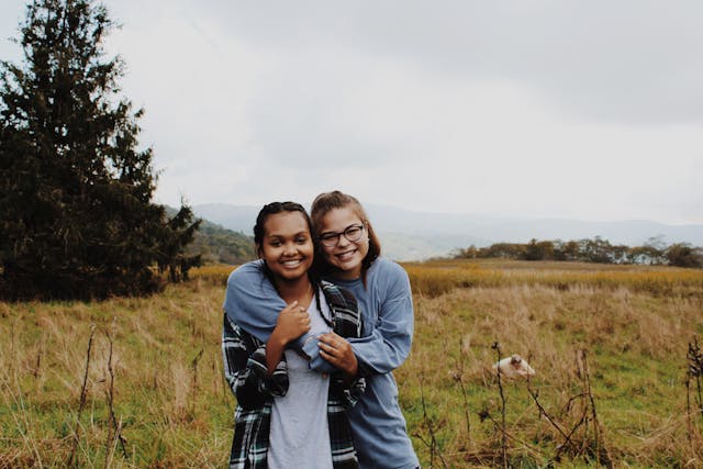 Two smiling friends standing in a grassy field, embracing and showing their close bond. The image captures the essence of making your quinceañera court, including damas and chambelanes, feel special by emphasizing friendship, appreciation, and gratitude for their role in your celebration.