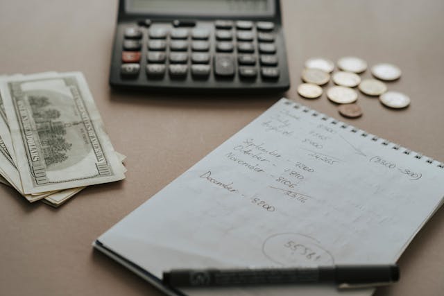 A calculator, a stack of cash, coins, and a notepad with handwritten budgeting details sit on a table. The image emphasizes the importance of setting a clear budget before hiring a quinceañera choreographer to ensure costs are manageable and aligned with your overall event planning.