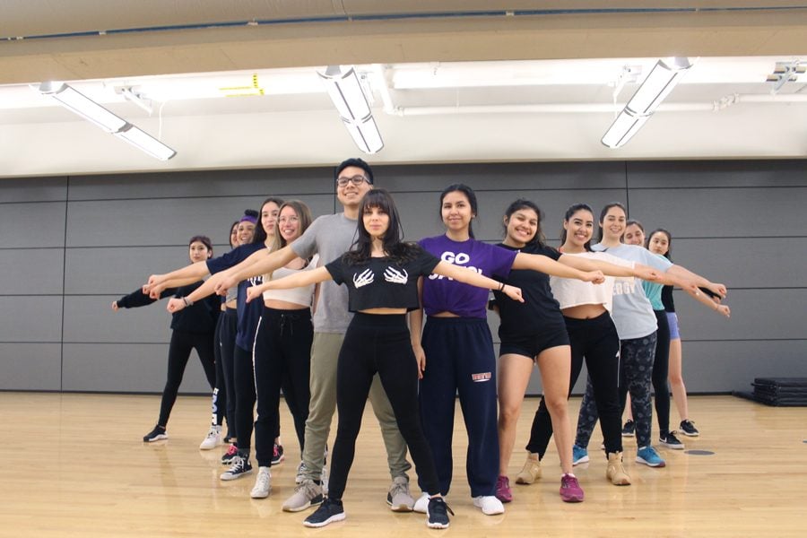 A group of quinceañera court members rehearsing a dance routine in a studio. The participants are aligned in formation with their arms outstretched, smiling and practicing together, emphasizing the teamwork and preparation needed to avoid a quinceañera dance disaster.