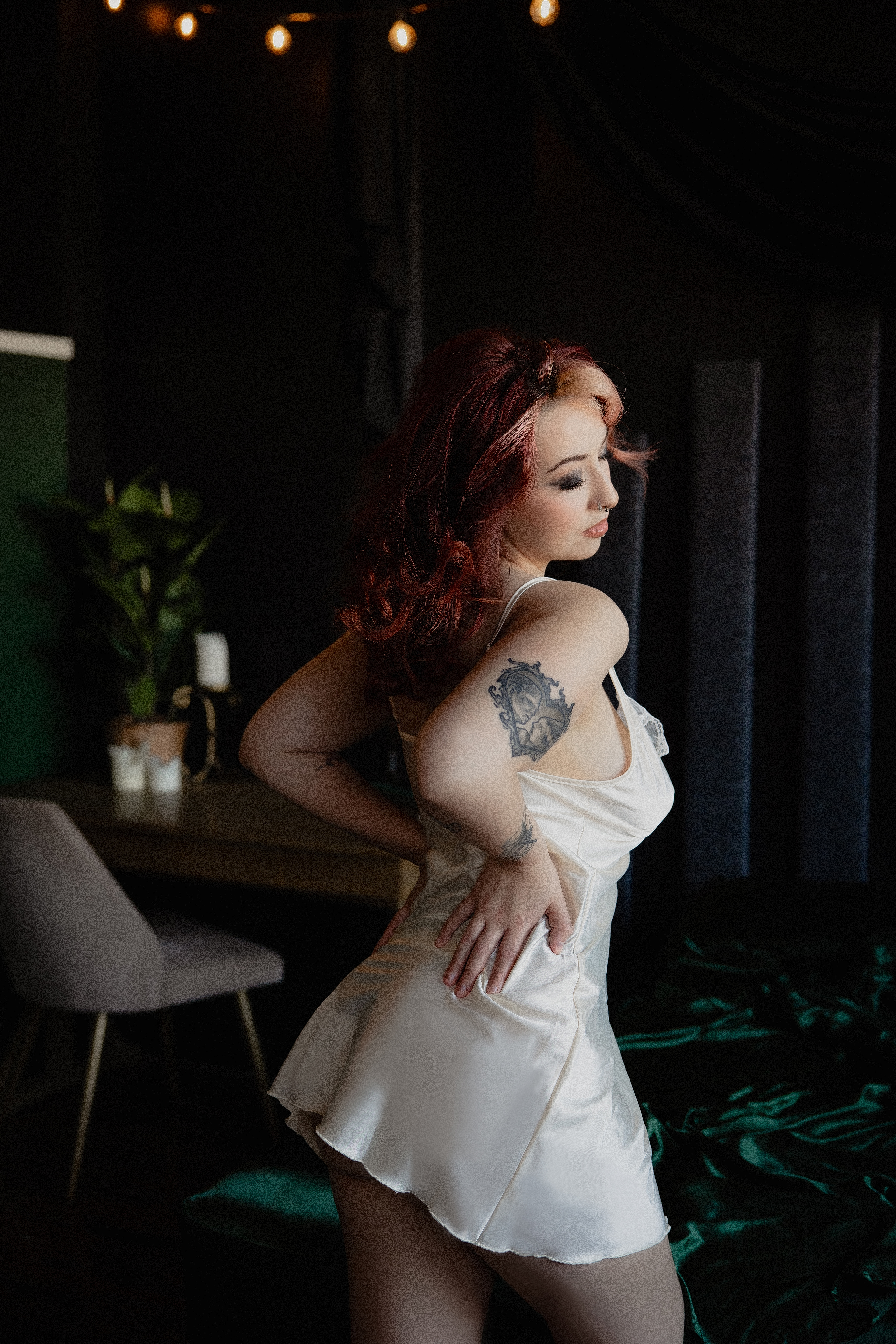 Boudoir portrait of a woman in a satin slip dress posing in soft indoor light.