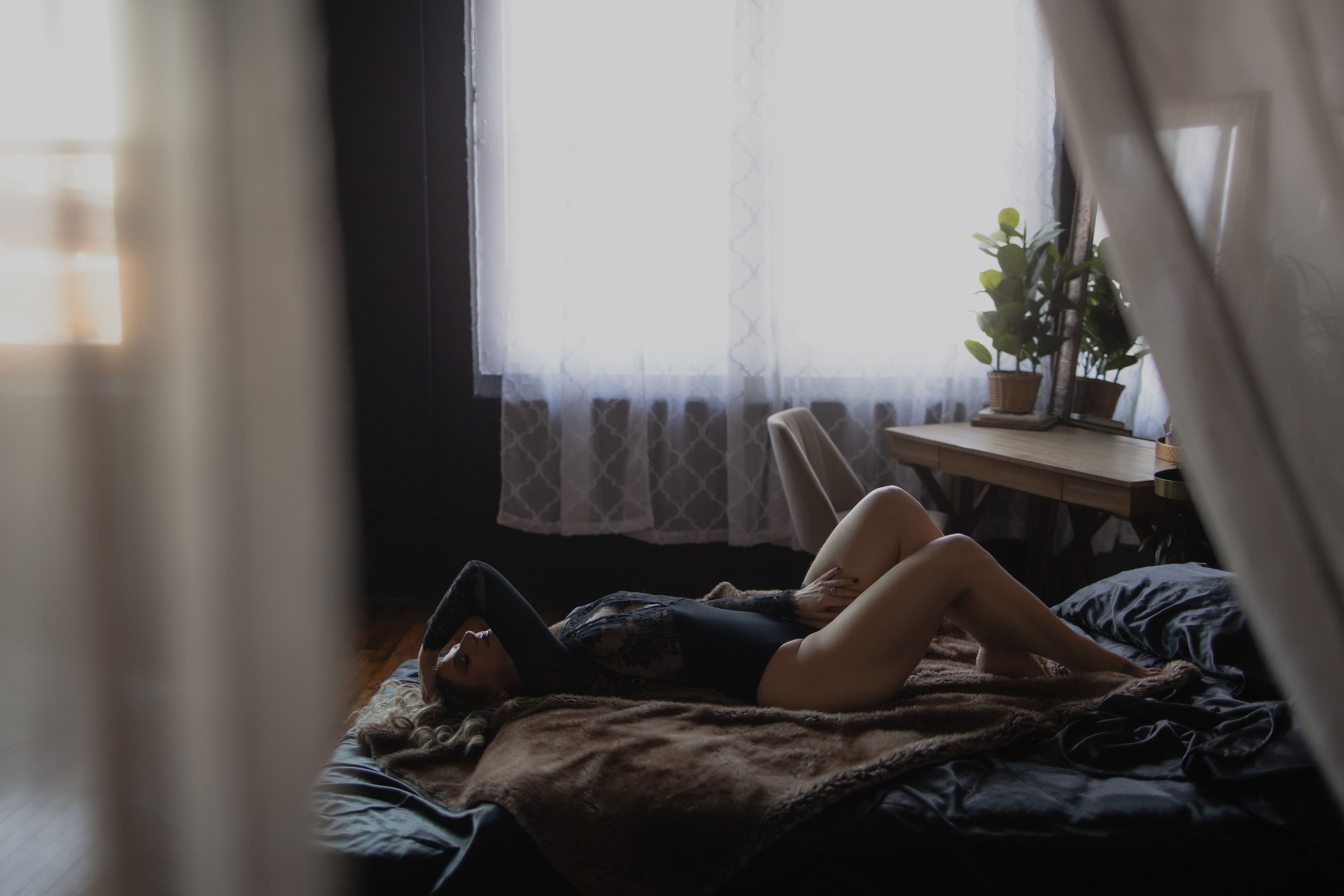 Natural-light boudoir photography of a woman reclining in black lace lingerie inside a cozy, intimate studio.