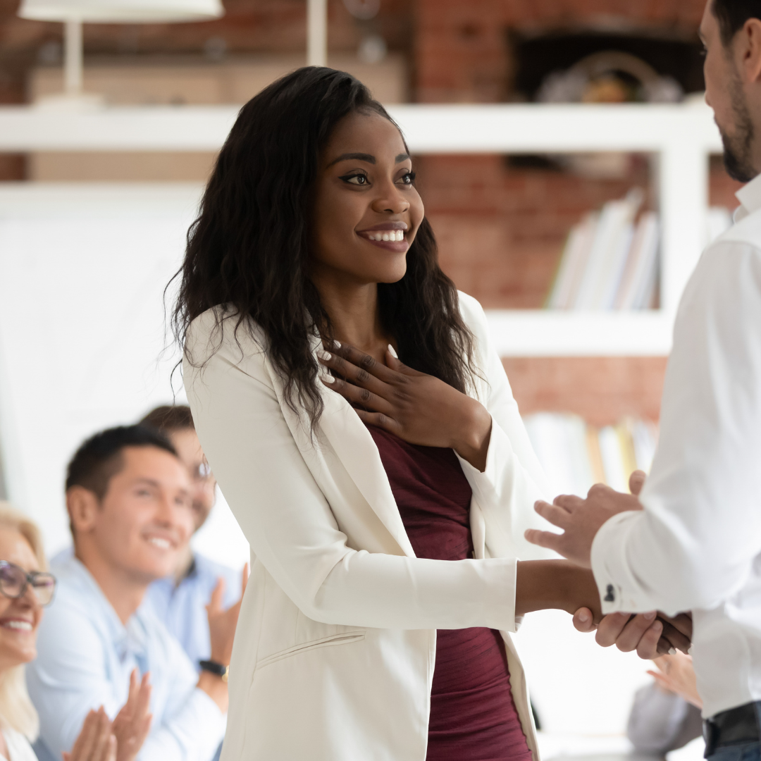 African american woman shakes supervisors hand and looks shocked to be rewarded.