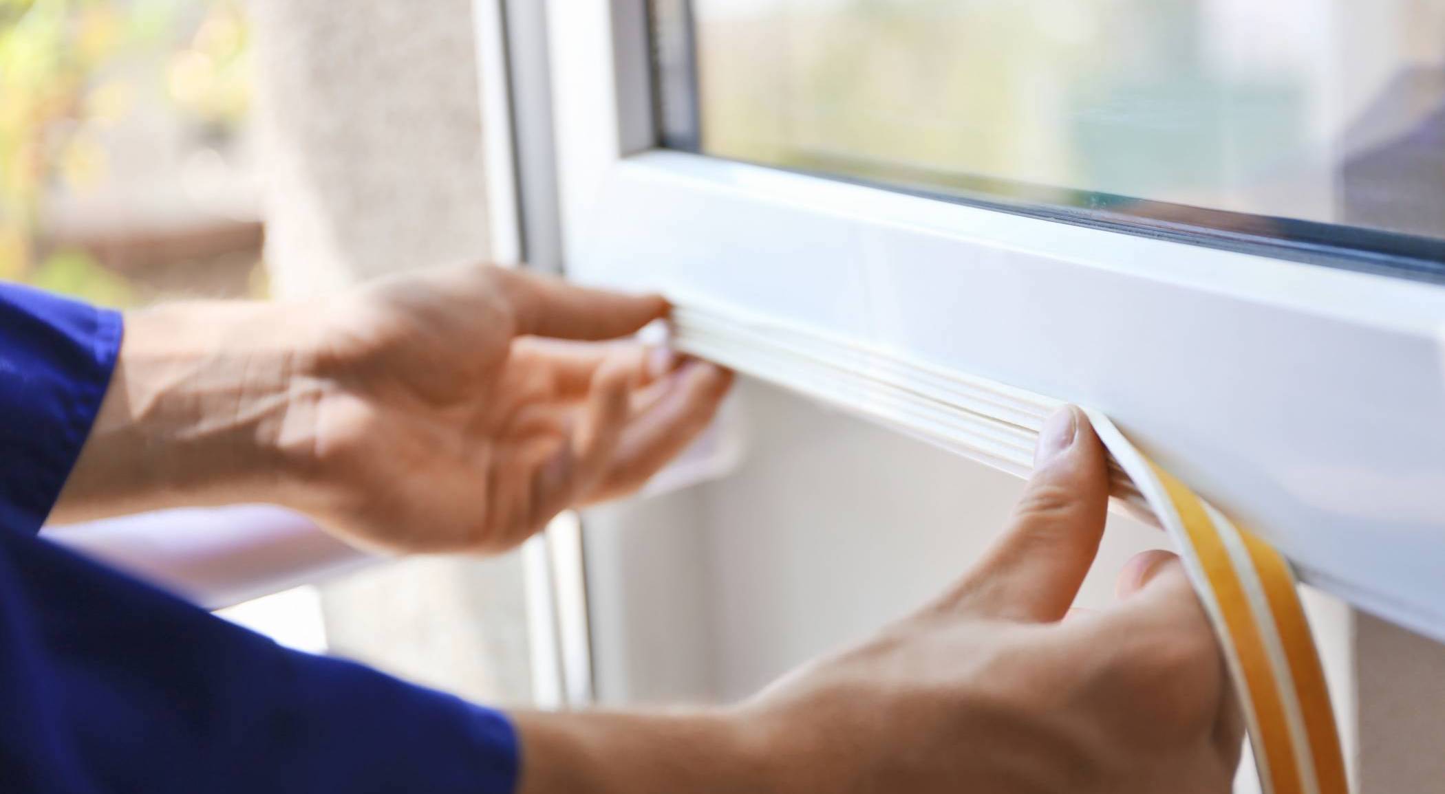 a person's hands putting a white plastic window seal on a window