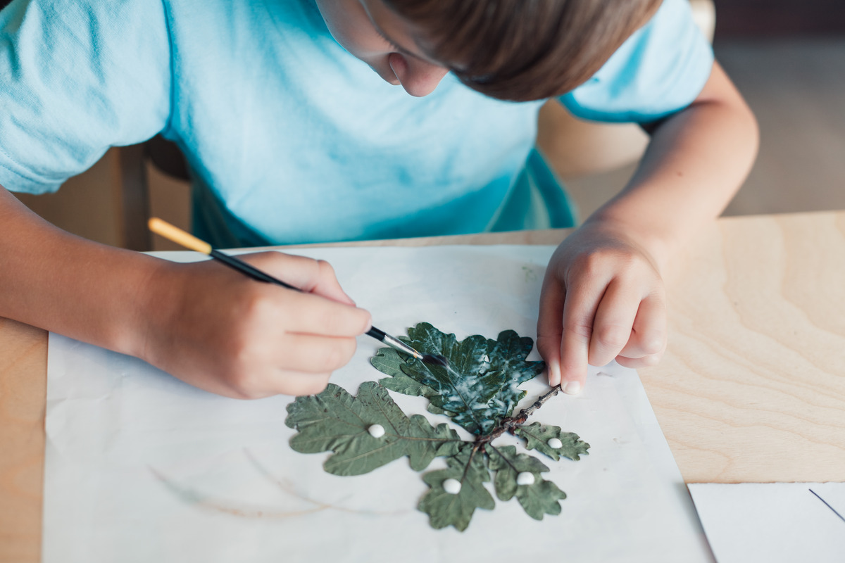 kid gluing leaves in summer nature collage