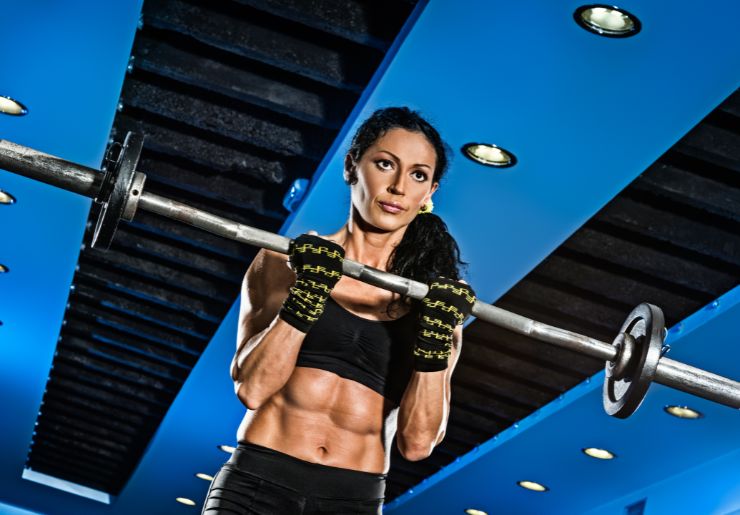 Athletic woman curling barbell in a gym with blue ceiling and dramatic lighting