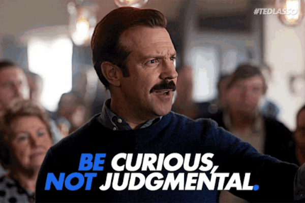 Ted Lasso throwing darts with words saying Be curious not judgmental.