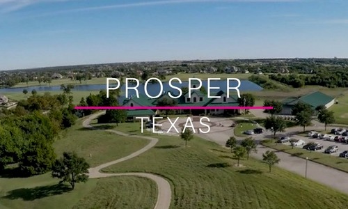Aerial view of a scenic park and residential area in Prosper, Texas, with a lake, walking trails, green spaces, and the words “Prosper Texas” overlaid in white and pink text.
