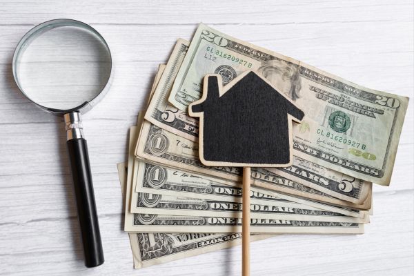Stack of dollar bills with a house icon and magnifying glass. Stack of dollar bills with a house icon and magnifying glass.