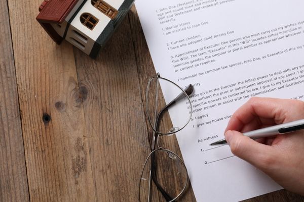 Hand signing a legal document next to eyeglasses and a small house model. Hand signing a legal document next to eyeglasses and a small house model.