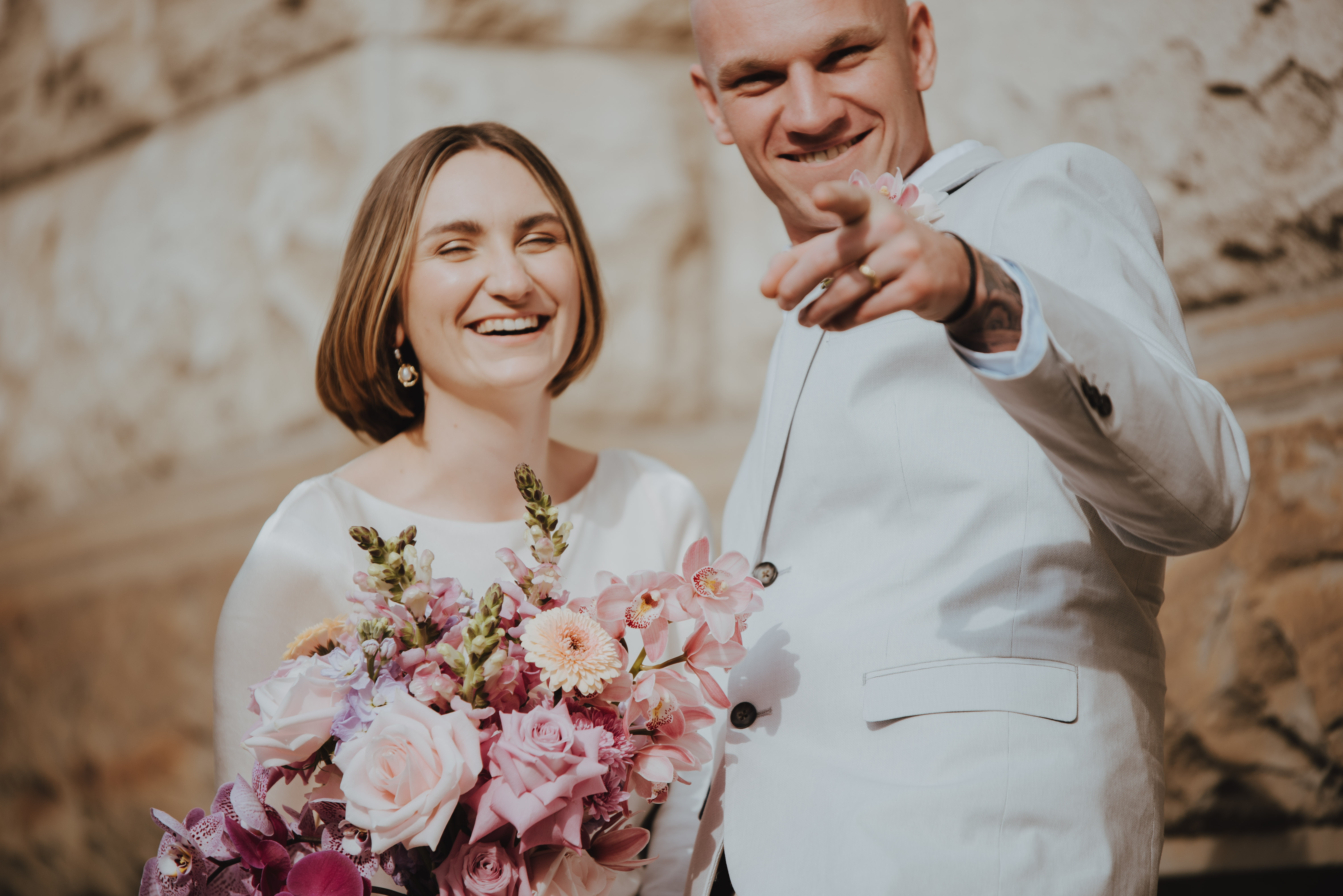 groom pointing at the camera while bride laughs