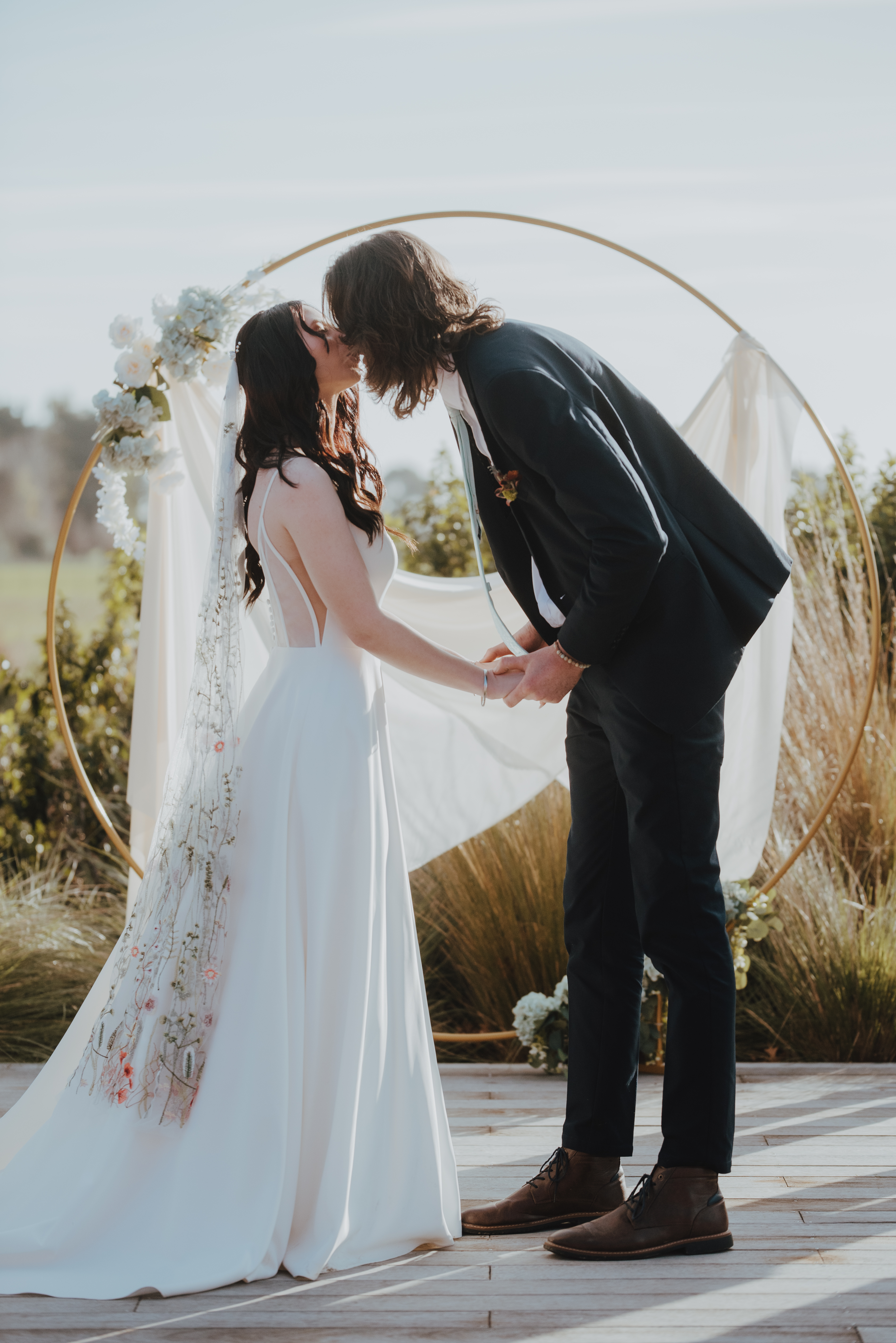 first kiss at wedding ceremony with hoop style arch