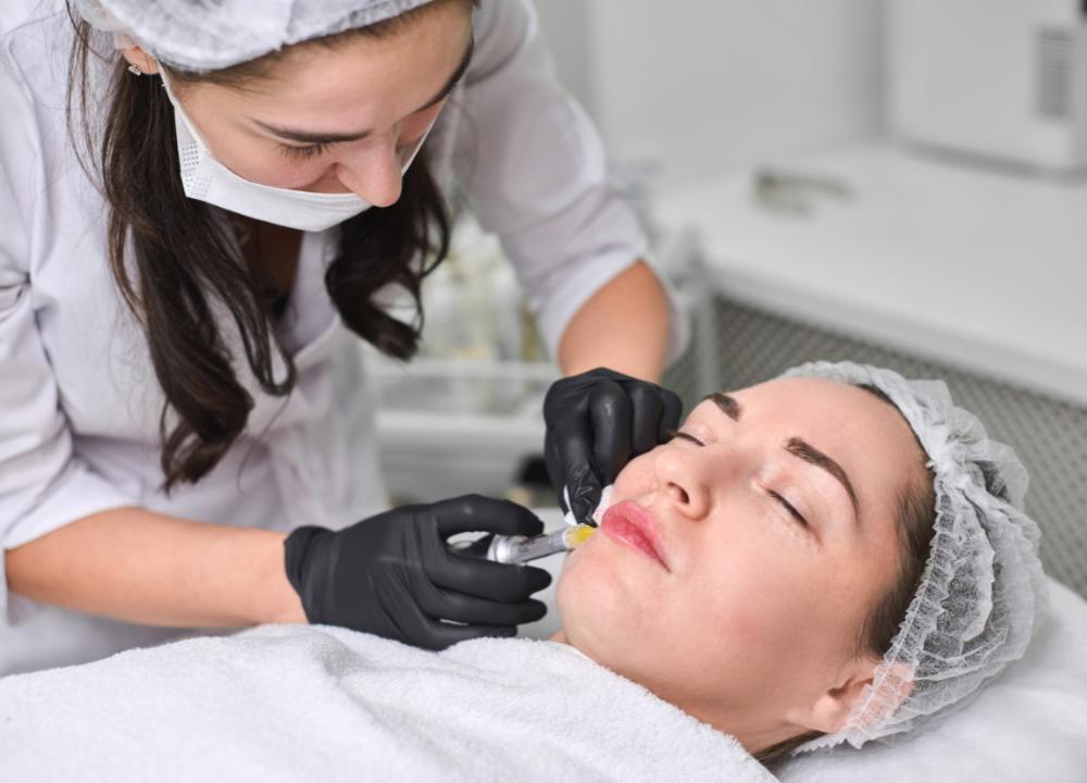Medical aesthetician performing precision lip filler injection on patient in professional dermatology clinic setting.