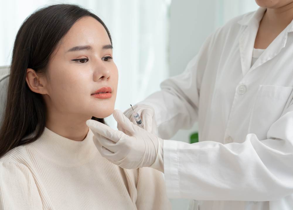 Woman receiving Kybella injection under the chin for fat reduction, showing non-surgical double chin contouring treatment.