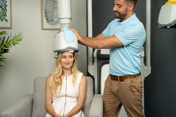 Happy female patient receiving TMS Treatment from a traditional helmet device by doctor