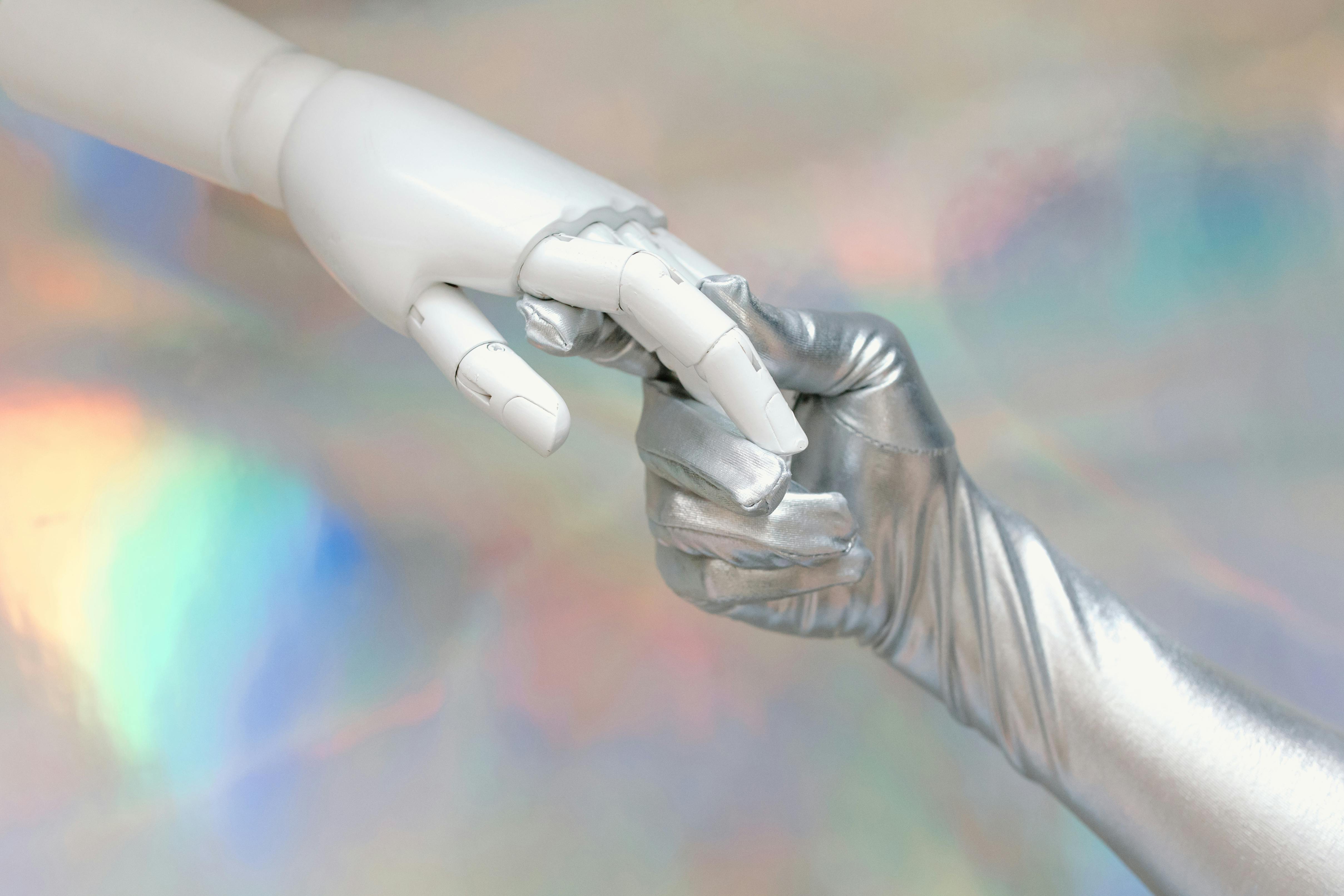Silver human hand gently holding a white robotic hand, symbolising how over-relying on AI for validation can disconnect us from our own creative brilliance.