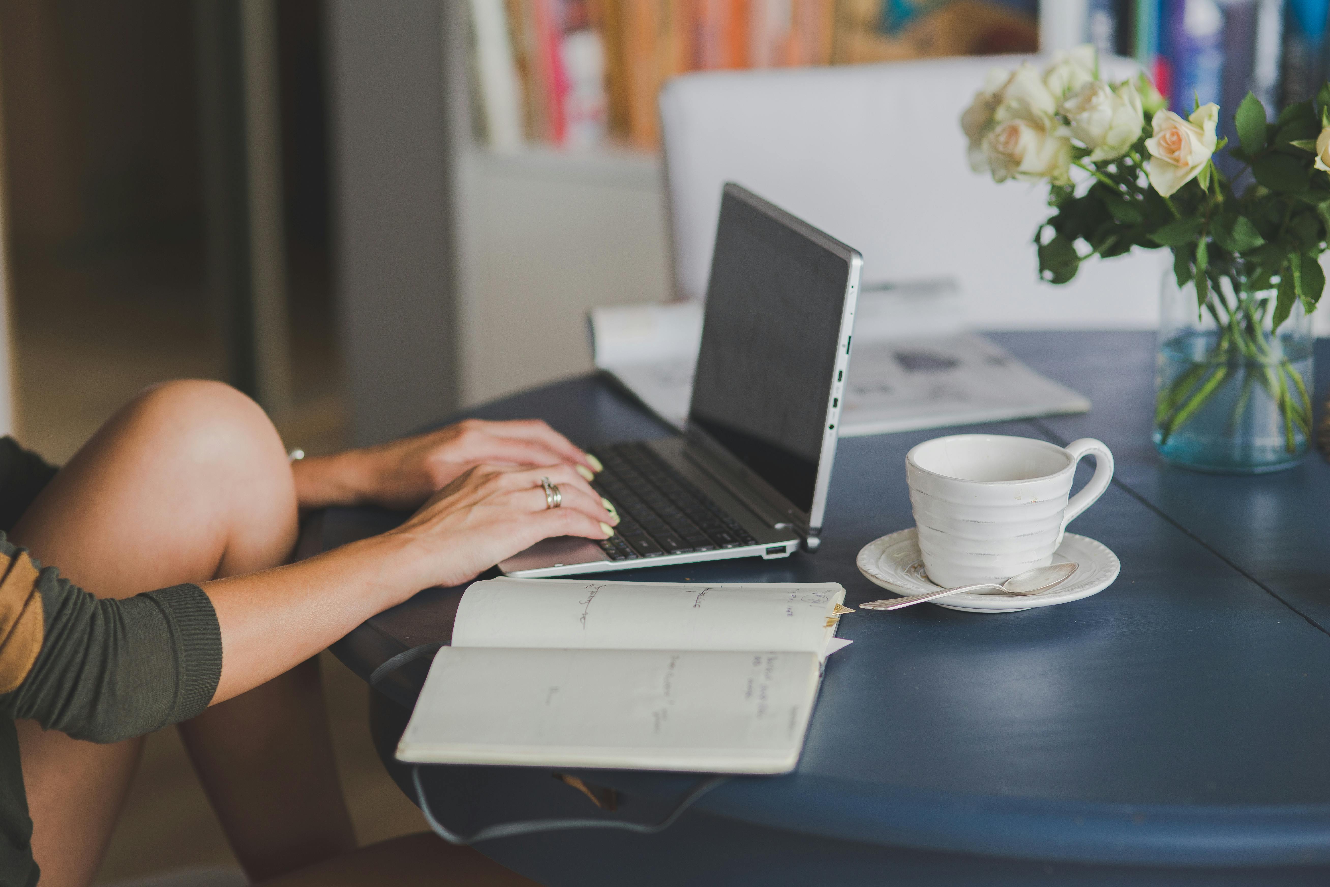 Person typing on a laptop with a coffee and open notebook nearby — capturing the quiet focus of creating ideas before seeking outside validation.
