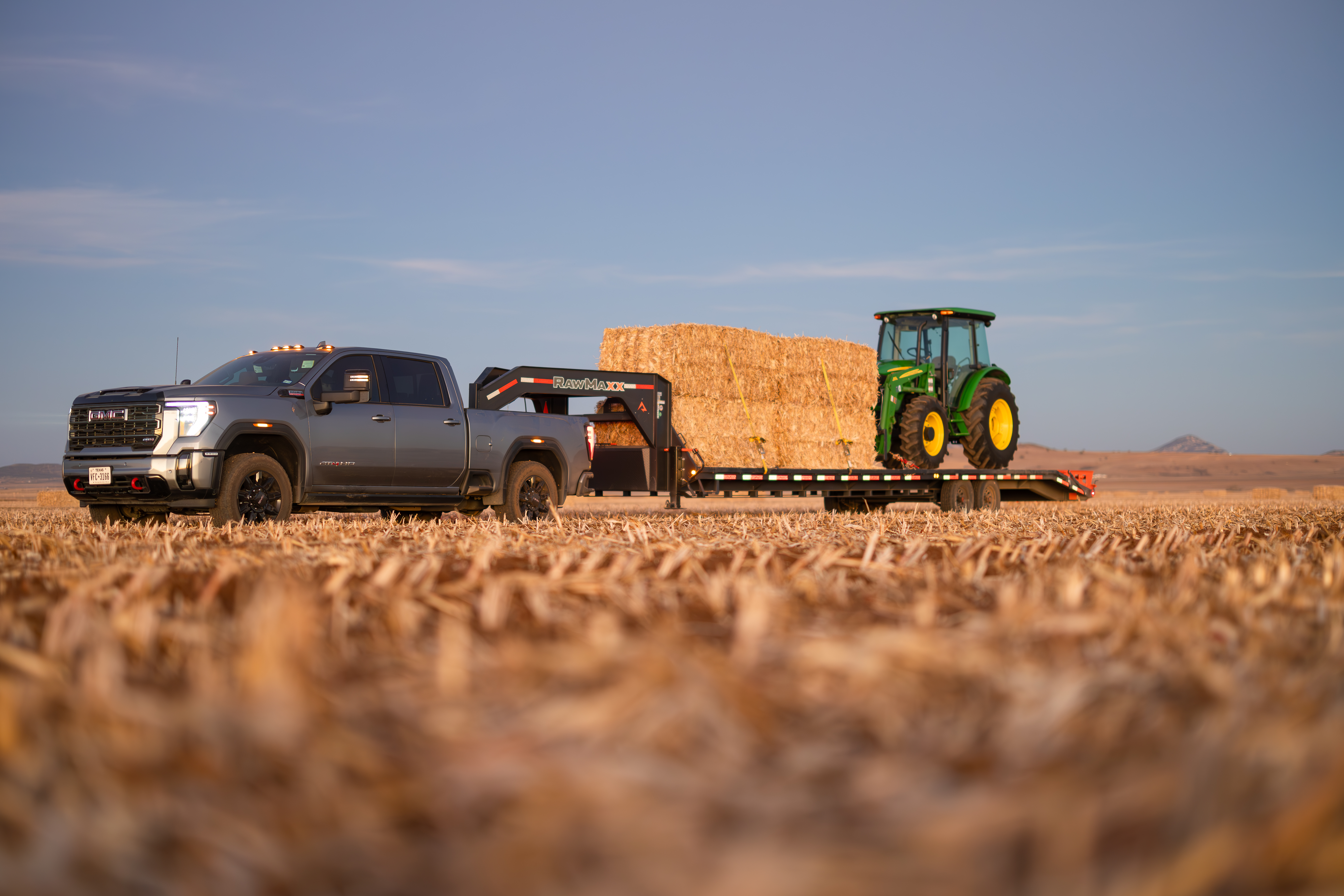 RawMaxx FDX Dual gooseneck trailer loaded with hay bales and a tractor, showcasing its heavy-duty capacity and stability for farm and agricultural hauling. RawMaxx FDX Dual gooseneck trailer loaded with hay bales and a tractor, showcasing its heavy-duty capacity and stability for farm and agricultural hauling.