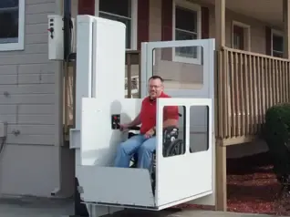A person in a wheelchair using an outdoor wheelchair lift, also known as a vertical platform lift.