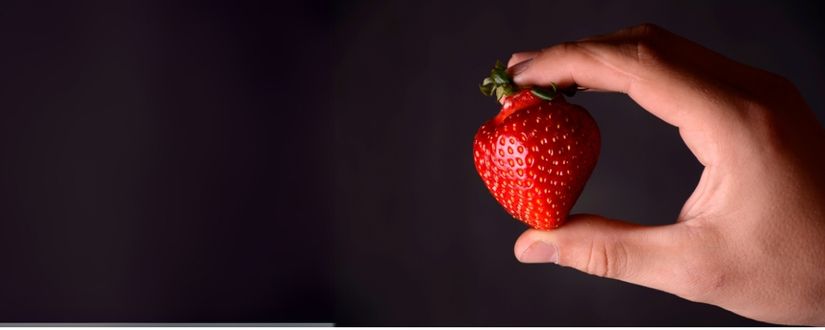 Hand holding a fresh strawberry against a dark background, highlighting how even healthy-looking foods can be hidden triggers for food sensitivities. Hand holding a fresh strawberry against a dark background, highlighting how even healthy-looking foods can be hidden triggers for food sensitivities.