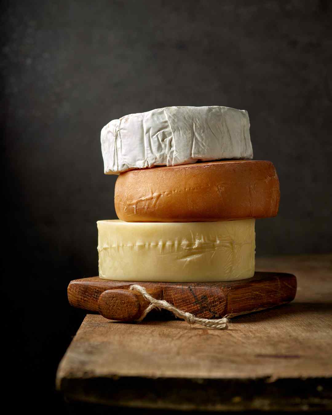 Three wheels of cheese stacked on a rustic wooden board, symbolizing dairy—a common trigger for food intolerances. Three wheels of cheese stacked on a rustic wooden board, symbolizing dairy—a common trigger for food intolerances.