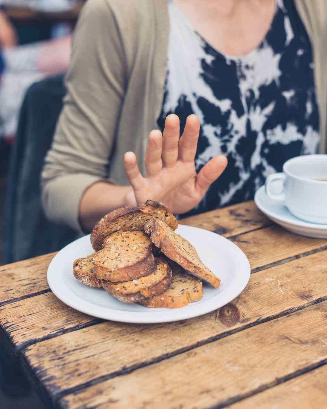Person pushing away a plate of whole grain bread, symbolizing gluten avoidance due to celiac disease or gluten sensitivity. Person pushing away a plate of whole grain bread, symbolizing gluten avoidance due to celiac disease or gluten sensitivity.