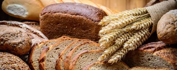 Assortment of whole grain and wheat breads with wheat stalks, representing common gluten-containing foods that can trigger symptoms in people with celiac disease, non-celiac gluten sensitivity, or wheat allergies. Assortment of whole grain and wheat breads with wheat stalks, representing common gluten-containing foods that can trigger symptoms in people with celiac disease, non-celiac gluten sensitivity, or wheat allergies.