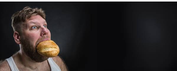 Man with a shocked expression holding a whole bread roll in his mouth—symbolizing the overwhelming and confusing nature of hidden food reactions and the modern diet’s impact on the body. Man with a shocked expression holding a whole bread roll in his mouth—symbolizing the overwhelming and confusing nature of hidden food reactions and the modern diet’s impact on the body.