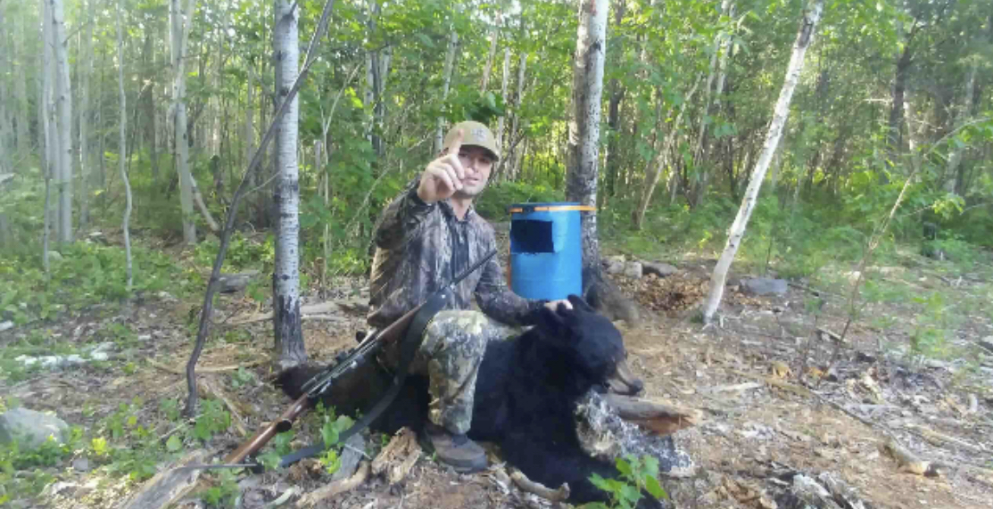 Chief Little Eagle (Pat Gatz) sitting on a bear he hunted in the woods, wearing hunting attire and pointing towards the camera. Chief Little Eagle (Pat Gatz) sitting on a bear he hunted in the woods, wearing hunting attire and pointing towards the camera.