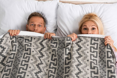 Couple in bed with the blankets pulled up to their chins. Couple in bed with the blankets pulled up to their chins.
