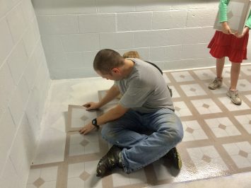 man laying peel and stick tile on a basement floor