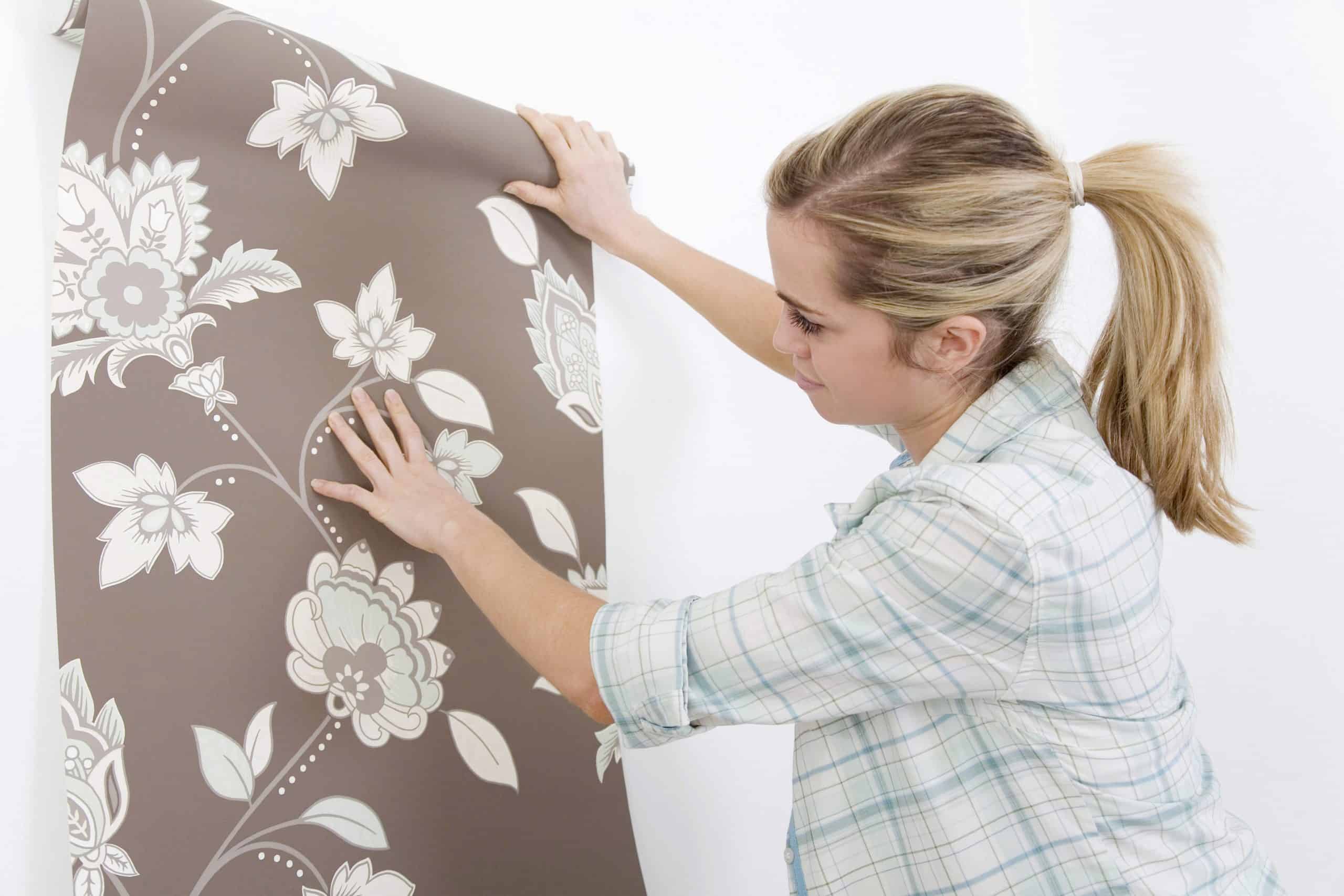 woman holding up wallpaper to a wall