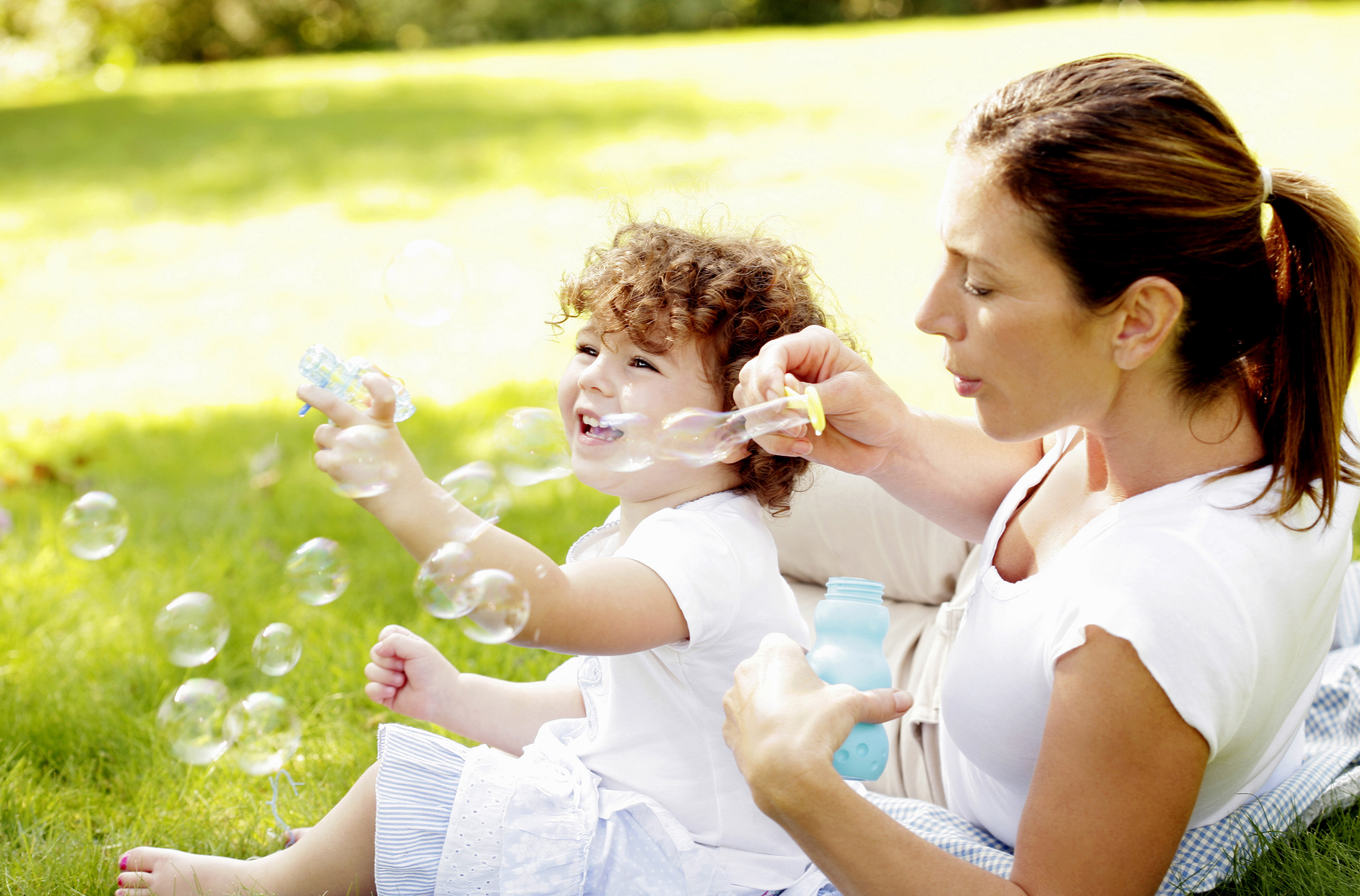 mom and young child smiling and blowing bubbles together